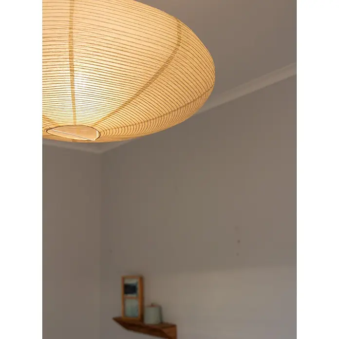 PR Home Pendelleuchte Lampenschirm beige -  - Eine beleuchtete, gerippte Deckenleuchte im Papierlaternen-Stil hängt in einem Raum und spendet warmes Licht.