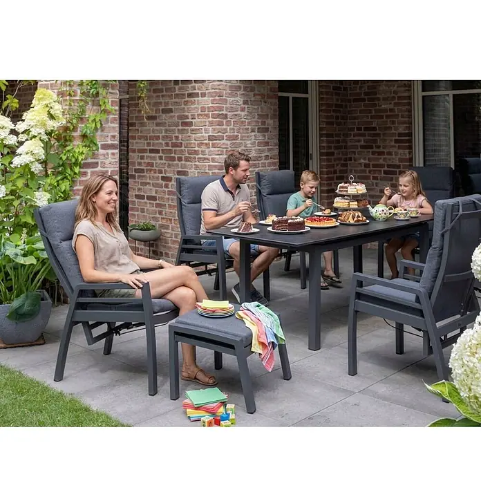 Bene Living Gartentisch-Set Merida + Hocker mit Tisch Tarifa - Gesamtumfang: 8 -tlg., Aluminium pulverbeschichtet, Textilene, Keramik, Rückenlehne verstellbar - Dunkelgraue Outdoor-Esstischgarnitur mit gepolsterten Stühlen und Tisch, von einer Familie auf der Terrasse genutzt.