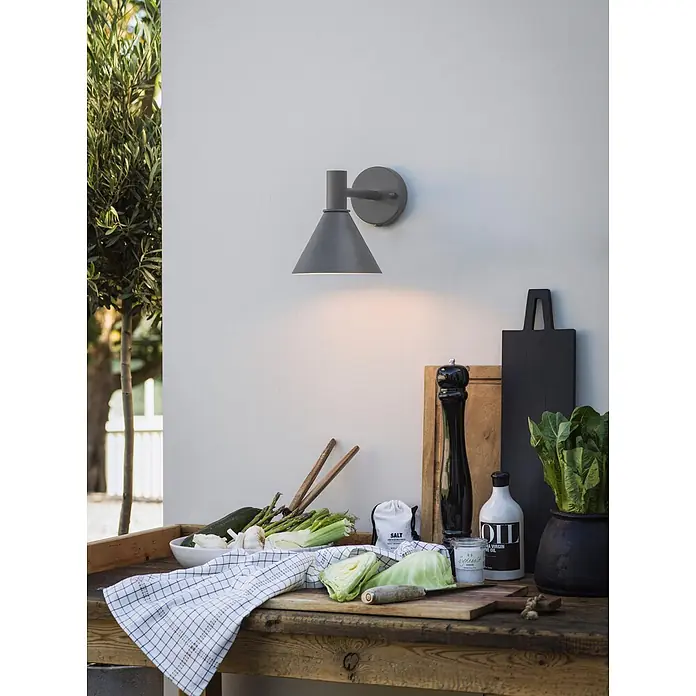 PR Home Außenwandleuchte Mini-Tripp - 15 W, IP44 - Graue, kegelförmige Wandleuchte beleuchtet einen Kochbereich im Freien mit frischem Gemüse auf einem Holztisch.