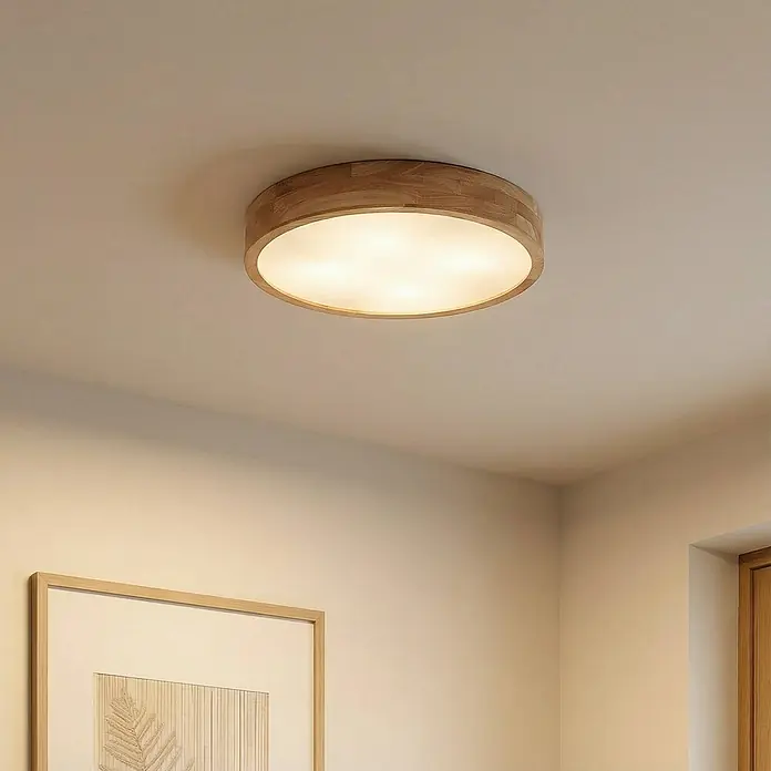 Lindby Deckenleuchte Tanju - Holz hell, E27 - Runde Deckenleuchte mit hellem Holzrahmen und weißem Diffusor, in einem Raum montiert.