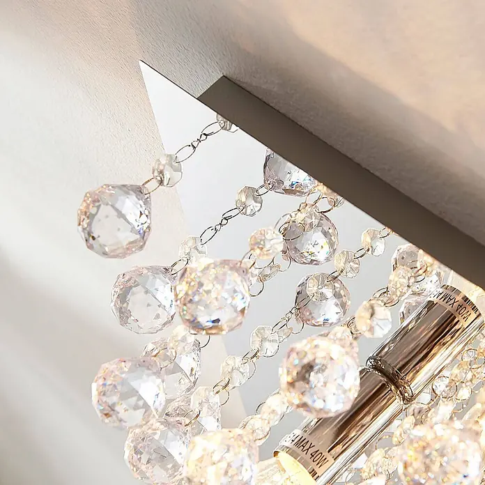Lindby Deckenleuchte Annica - chrom / silber, klar / transparent, E14 - Nahaufnahme einer Deckenleuchte mit funkelnden klaren facettierten Kristallen und einem silberfarbenen Metallsockel mit sichtbarer Glühbirne.
