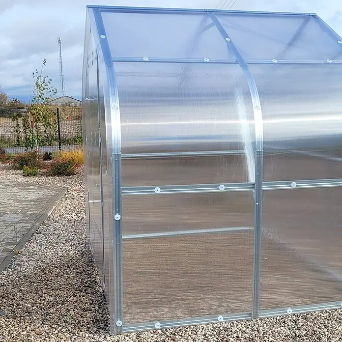 Klasika Greenhouses Gewächshaus Drop Klasika - Außenmaß inkl. Dachüberstand (B x T): 250 x 200 cm, Material Seitenwand: Kunststoff, 4 mm, Silbergrau - Ein transparentes Gewächshaus aus gewelltem Polycarbonat mit silbernem Metallrahmen, auf Kies im Freien stehend.