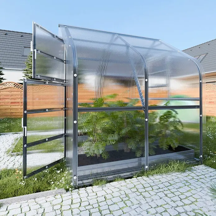 Klasika Greenhouses Gewächshaus Drop Klasika - Außenmaß inkl. Dachüberstand (B x T): 250 x 200 cm, Material Seitenwand: Kunststoff, 4 mm, Silbergrau - Ein transparentes Polycarbonat-Gewächshaus mit dunklem Rahmen, Pflanzen enthaltend, steht auf einer Steinterrasse im Garten.