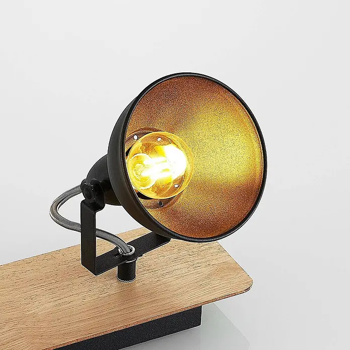 Lindby Deckenstrahler Aylis - Holz dunkel, schwarz, E14 - Schwarze Metall-Spotlampe mit goldener Innenseite und sichtbarer Glühbirne, auf hellem Holzsockel.