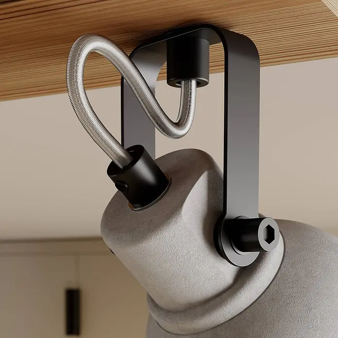 Lindby Deckenstrahler Mitis - Holz dunkel, alu / grau / zink, GU10 - Nahaufnahme eines grauen, strukturierten Lampenkopfes mit schwarzer Metallhalterung und flexiblem silbernem Kabel unter einer Holzoberfläche montiert.