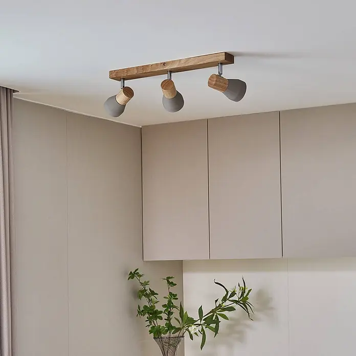 Lindby Deckenstrahler Filiz - Holz hell, alu / grau / zink, E14 - Deckenleuchte mit Holzleiste und drei grauen, konischen Spots, über Schränken montiert.