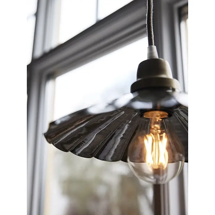 PR Home Pendelleuchte Ester - 25 W, E27 - Eine Nahaufnahme einer Hängelampe mit dunklem, gewelltem Metallschirm und klarer, warm leuchtender Glühbirne.