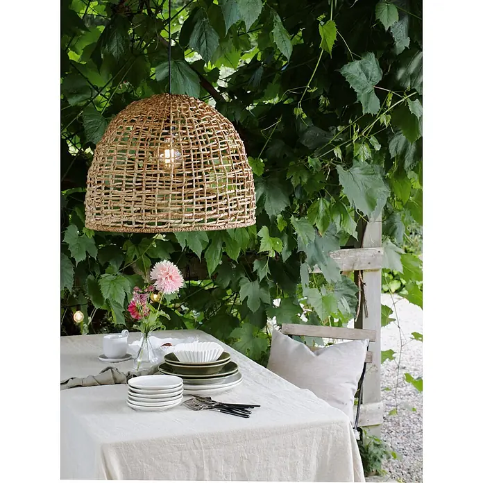 PR Home Pendelleuchte 57cm Outdoor - 40 W, E27 - Eine glockenförmige Hängelampe aus geflochtener Naturfaser über einem Esstisch im Freien.