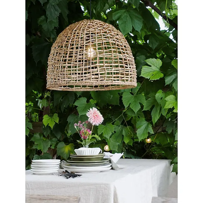 PR Home Pendelleuchte 57cm Outdoor - 40 W, E27 - Geflochtene Pendelleuchte aus Naturmaterial, hängt über einem gedeckten Esstisch im Freien.