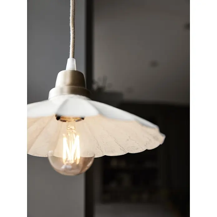 PR Home Pendelleuchte Ester - 25 W, E27 - Pendelleuchte mit plissiertem weißem Schirm, Messingfassung und leuchtender Filamentbirne, hängt in einem Innenraum.