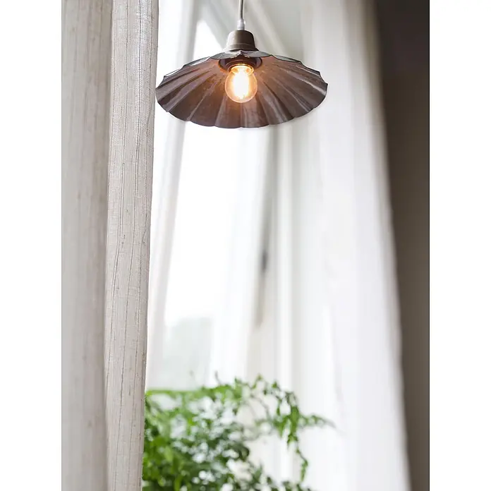 PR Home Pendelleuchte Ester - 40 W, E27 - Vintage-Pendelleuchte aus geriffeltem Metall mit freiliegender Glühbirne, hängt in einem hellen Raum mit transparenten Vorhängen.