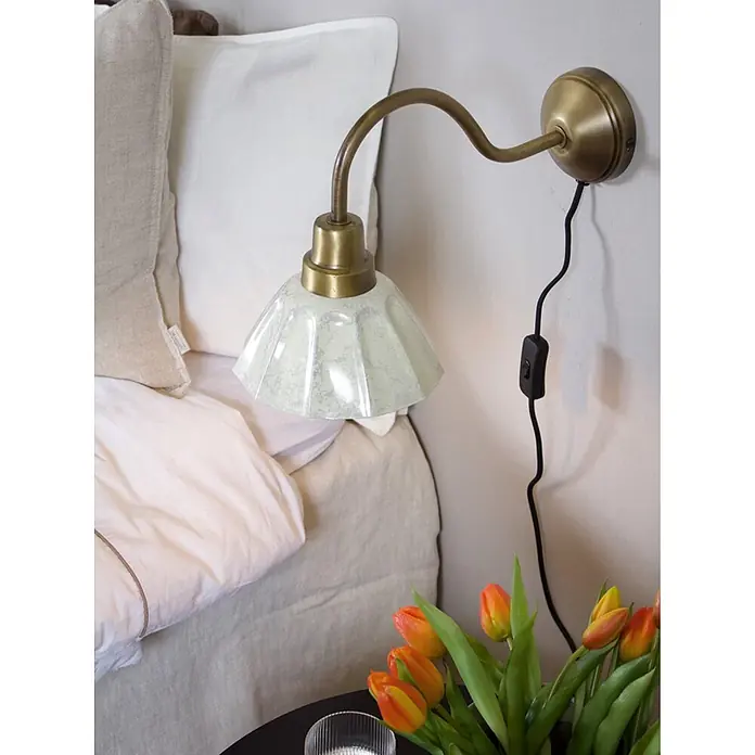 PR Home Pendelleuchte Ester - 25 W, E27 - Wandmontierte Messinglampe mit hellgrünem plissiertem Schirm, neben einem Bett eingesteckt.