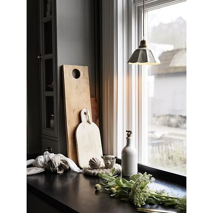PR Home Pendelleuchte Fensterleuchte - 15 W, E27 - Eine Küchenarbeitsplatte zeigt Holzschneidebretter, eine weiße Flasche, einen Schafbecher und frisches Grün, beleuchtet von einer Pendelleuchte am Fenster.