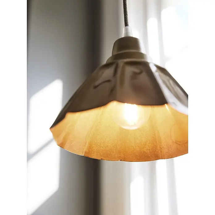 PR Home Pendelleuchte Ester - 25 W, E27 - Eine Pendelleuchte aus Metall mit strukturiertem Schirm und warm leuchtender Glühbirne hängt an einem geflochtenen Kabel.