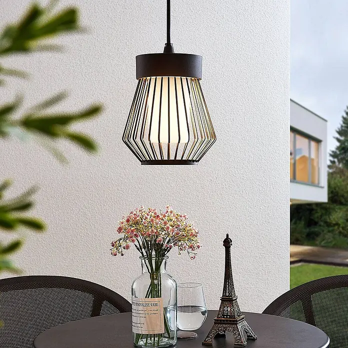 Lindby Außenwand- & Deckenleuchte Vajana - schwarz, IP44 - Schwarze Pendelleuchte mit geometrischem Metallgitter über einem Gartentisch mit Blumen und Eiffelturm-Deko.