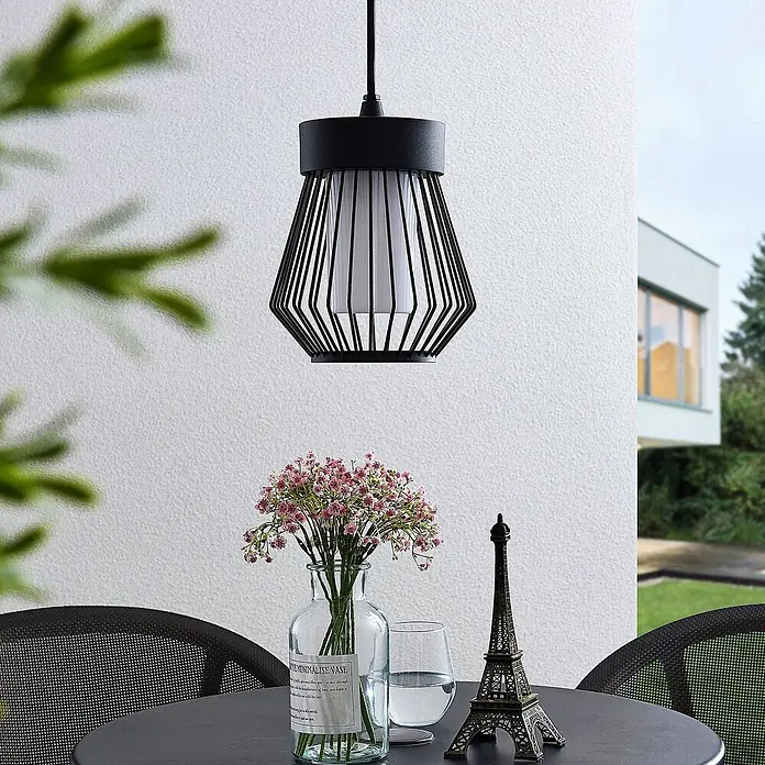 Lindby Außenwand- & Deckenleuchte Vajana - schwarz, IP44 - Schwarze geometrische Käfig-Pendelleuchte über einem Terrassentisch mit Blumen, einem Glas und einer Eiffelturmfigur.