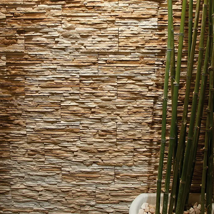 Revestimiento de piedra Galicia - Bronce, Cantidad total: 4 pzs. - Una pared con revestimiento de piedra decorativa en tonos marrones y beige, complementada con plantas de bambú, creando un ambiente elegante.