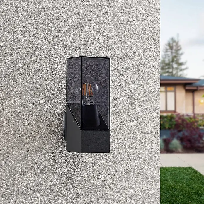 Lucande Außenwandleuchte Fiola - schwarz, IP54 - Schwarze Außenwandleuchte mit dunkeltransparentem Glasgehäuse und sichtbarer Edison-Birne, an strukturierter Wand montiert.
