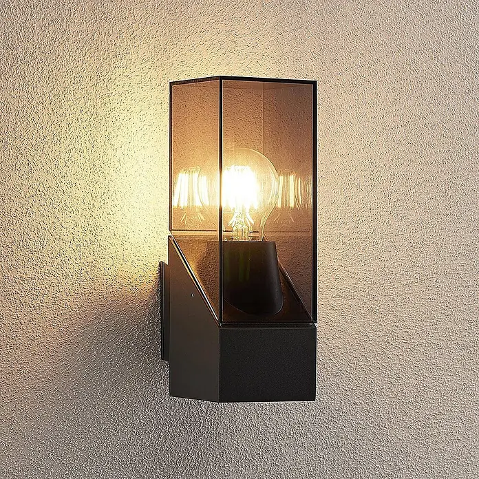 Lucande Außenwandleuchte Fiola - schwarz, IP54 - Schwarze Metall-Außenwandleuchte mit Rauchglas und leuchtender Filamentbirne, die Licht auf eine strukturierte Wand wirft.