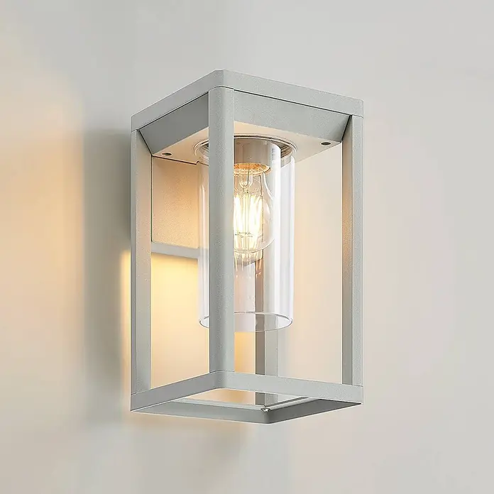 Lindby Wandleuchte aussen in silber, Aussenlampe Wand -  - Moderne graue Metall-Außenwandleuchte mit klarem Glaszylinder und warmer LED-Birne, an der Wand montiert.