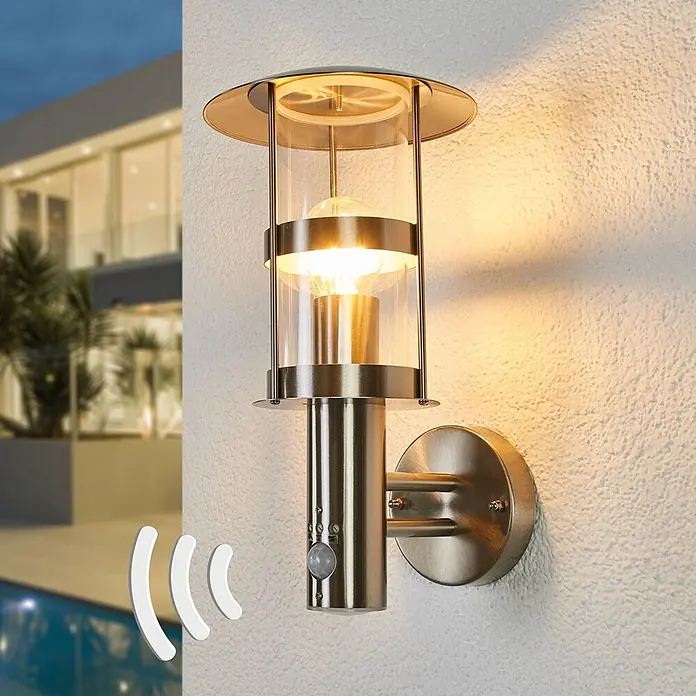 Lindby Außenwandleuchte Noemi - alu / grau / zink, alu / grau / zink, IP44 - Gebürstete Edelstahl-Außenwandleuchte mit Klarglas und Bewegungsmelder, beleuchtet an einer Außenwand.