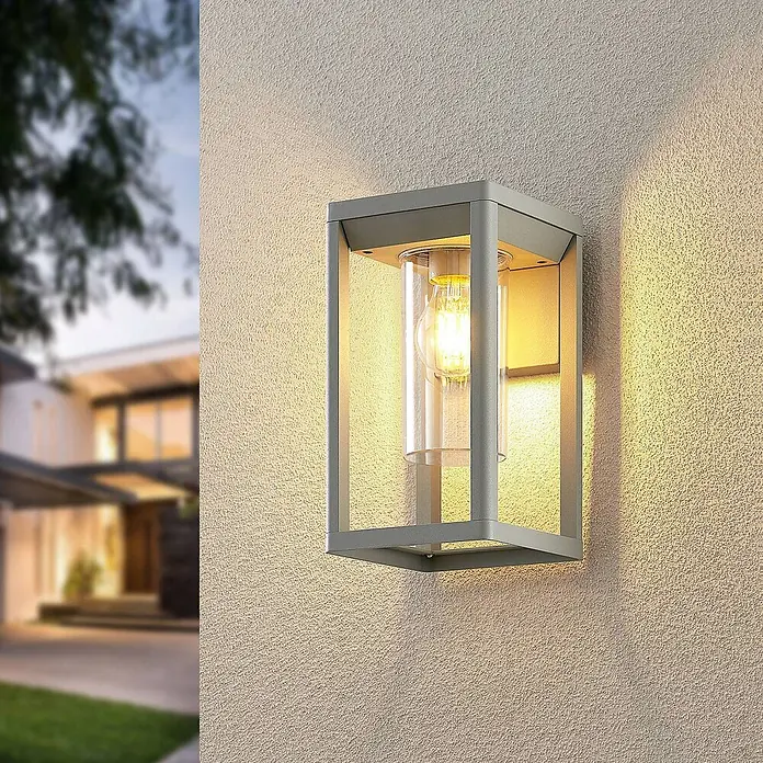 Lindby Wandleuchte aussen in silber, Aussenlampe Wand -  - Moderne graue Metall-Außenwandleuchte mit Klarglas und warmer LED-Birne, an einer strukturierten Hausaußenwand montiert.