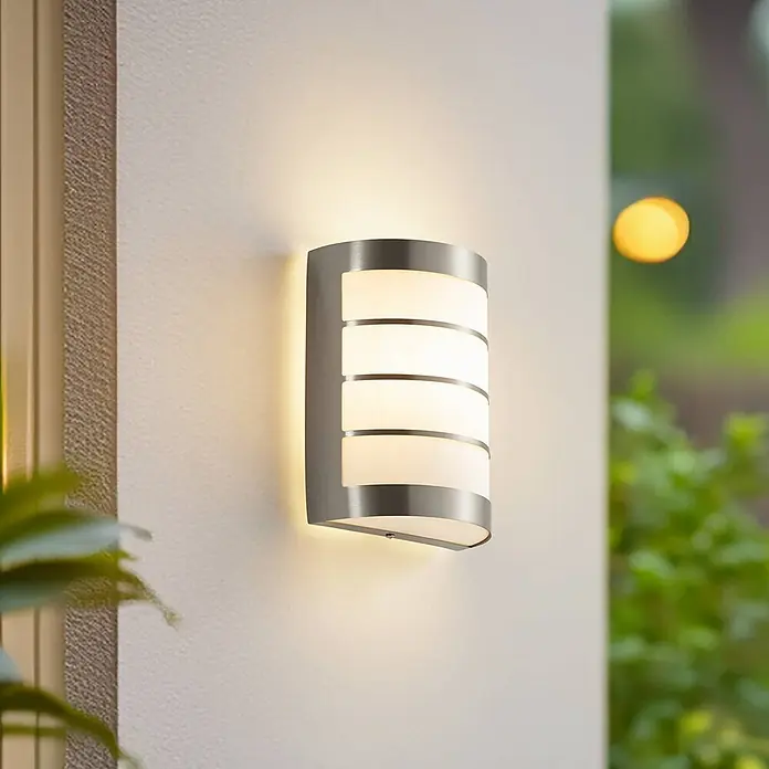 Lindby Außenwandleuchte Noyan - alu / grau / zink, alu / grau / zink, IP44 - Gebürstete Edelstahl-Außenwandleuchte mit mattierten weißen Diffusoren, leuchtend an einer Außenwand.