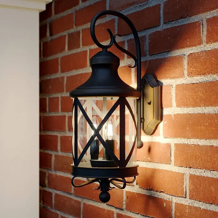 Lucande Außenwandleuchte Marcellino - braun / rost, braun / rost, IP23 - Schwarze traditionelle Außenwandlaterne mit klaren Glaspaneelen, die eine Ziegelwand beleuchtet.