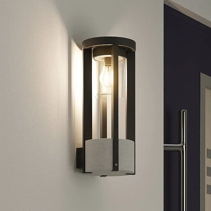 Lucande Außenwandleuchte Overa - alu / grau / zink, alu / grau / zink, IP44 - Wandleuchte aus schwarzem Metall und Klarglas mit Betonsockel, beleuchtet eine Wand.
