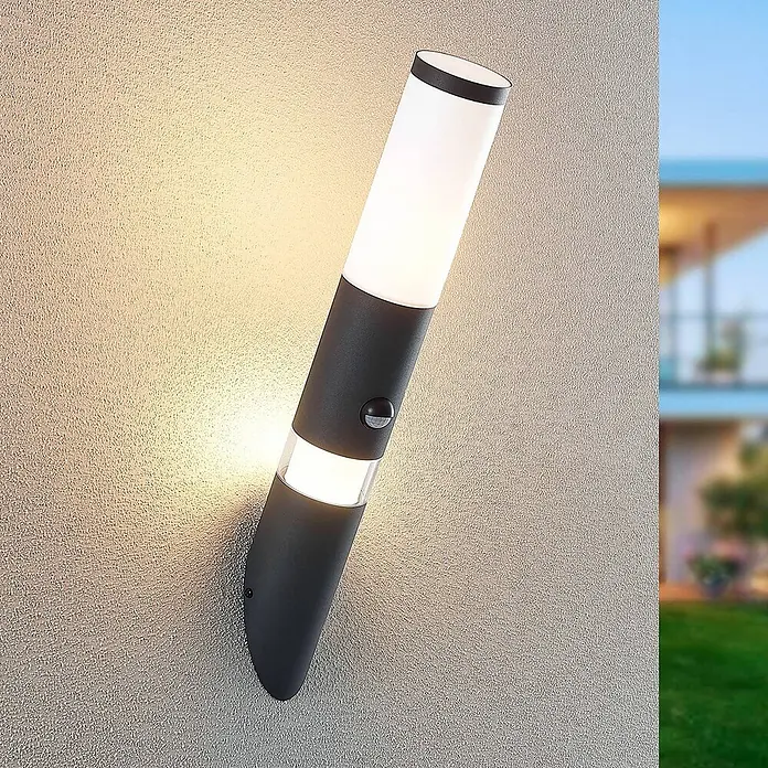 Lindby Außenwandleuchte Okari - schwarz, IP54 - Moderne anthrazitfarbene Außenwandleuchte mit Bewegungssensor, an einer strukturierten Wand montiert und beleuchtend.