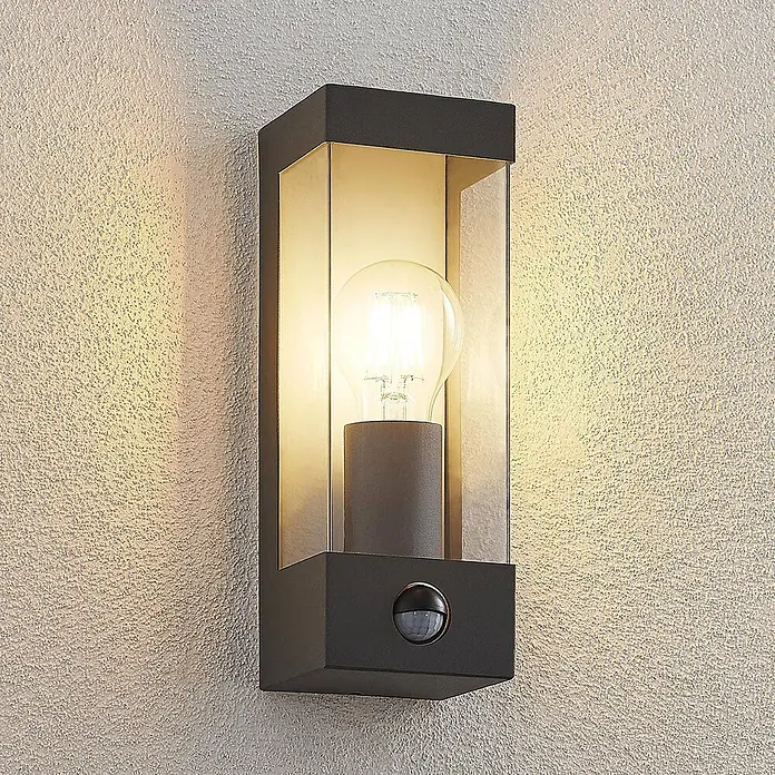 Lindby Außenwandleuchte Tilian - alu / grau / zink, alu / grau / zink, IP44 - Dunkelgraue Außenwandleuchte mit Klarglas und Bewegungsmelder, an strukturierter Wand montiert, leuchtet mit einer LED-Birne.