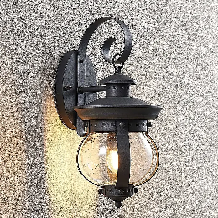 Lindby Außenwandleuchte Farley - 22 x 18,5 x 40 cm, schwarz, IP44 - Schwarze Außenwandleuchte aus Metall mit blasigem Glaskolben, an texturierter Wand montiert und beleuchtet.