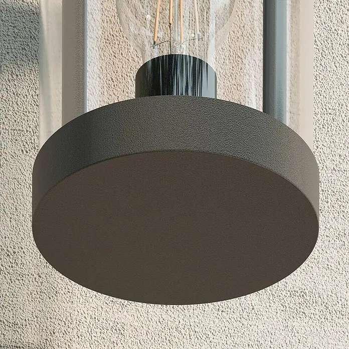 Lucande Außenwandleuchte Cassian - schwarz, IP54 - Dunkelgraue, texturierte Außenwandleuchte mit klarem Glasschirm und sichtbarer Glühlampe, an einer strukturierten Wand.