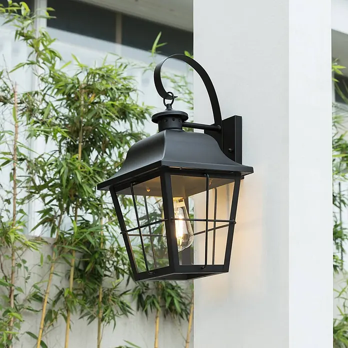 Lindby Außenwandleuchte Mertollio - 26,9 x 23,5 x 47,4 cm, schwarz, klar / transparent, IP43 - Schwarze Metall-Außenwandlaterne mit klaren Glaspaneelen und warmer LED-Glühlampe, an einem Pfeiler mit Bambus.