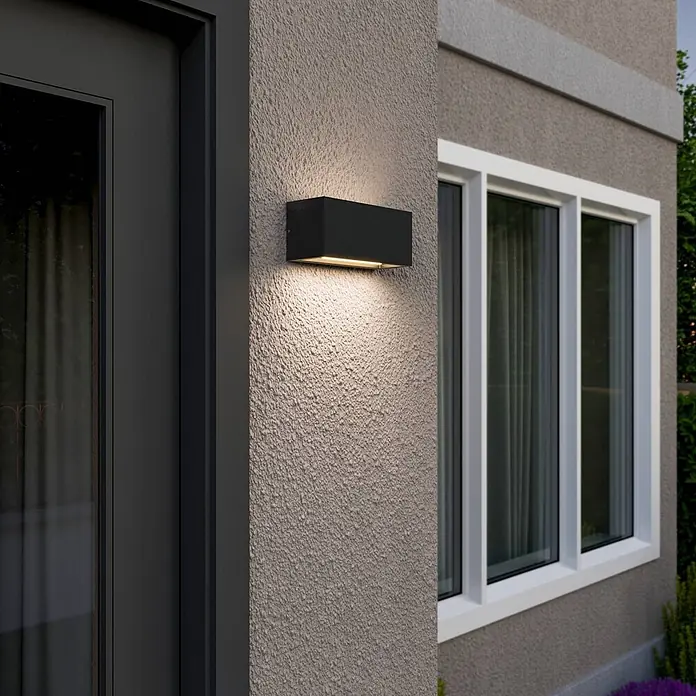 Lucande Außenwandleuchte Bente - schwarz, schwarz, IP54 - Schwarze rechteckige Außenwandleuchte beleuchtet eine strukturierte Wand neben Tür und Fenster.