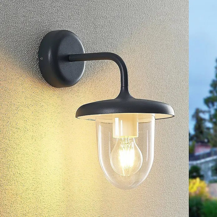 Prios Außenwandleuchte Larkumi - 24,7 x 18 x 30,3 cm, alu / grau / zink, IP54 - Dunkelgraue Außenwandleuchte mit klarem Glasschirm und warmer LED-Birne an einer strukturierten Wand.