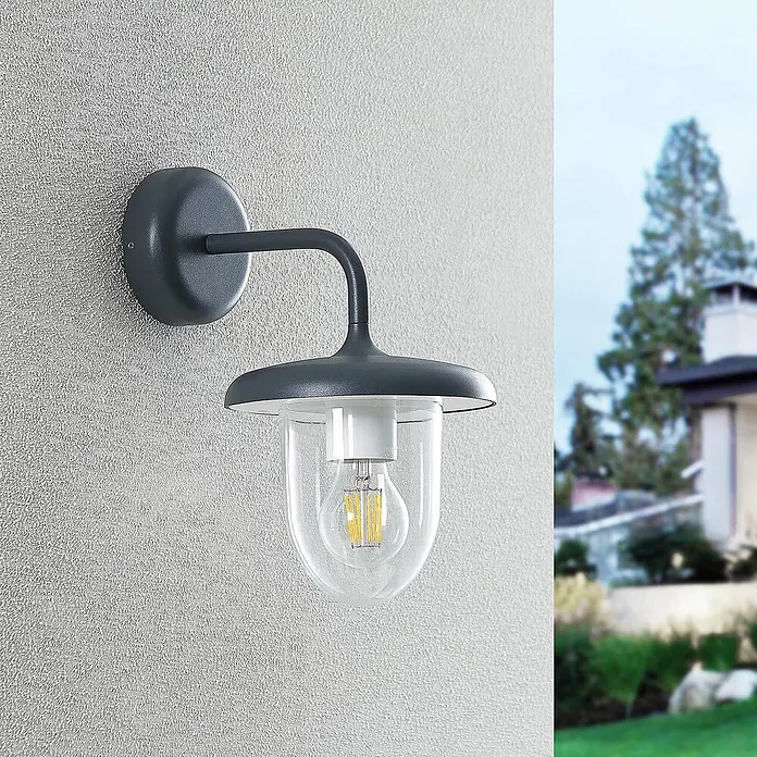 Prios Außenwandleuchte Larkumi - 24,7 x 18 x 30,3 cm, alu / grau / zink, IP54 - Dunkelgraue Außenwandleuchte mit Klarglas und LED-Birne, an strukturierter Wand montiert, Außenbereich im Hintergrund.