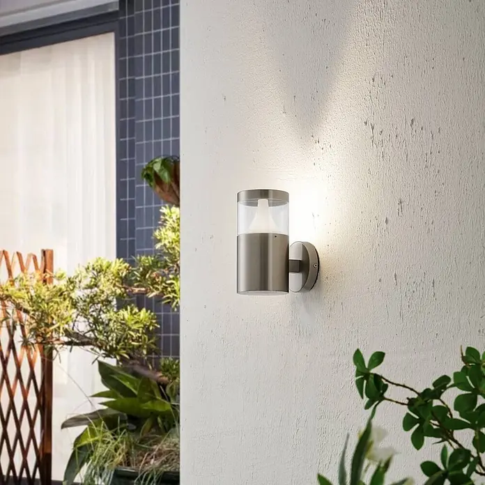Arcchio Außenwandleuchte Rudolfine - alu / grau / zink, alu / grau / zink, IP54 - Gebürstete Edelstahl-Außenwandleuchte mit klarem Glasschirm, an einer Wand montiert und beleuchtet.