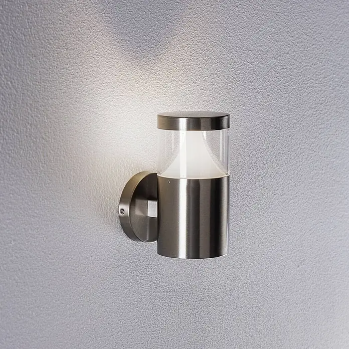 Arcchio Außenwandleuchte Rudolfine - alu / grau / zink, alu / grau / zink, IP54 - Gebürstete Edelstahl-Wandleuchte mit klarem und mattiertem Glasgehäuse, die eine strukturierte Wand beleuchtet.