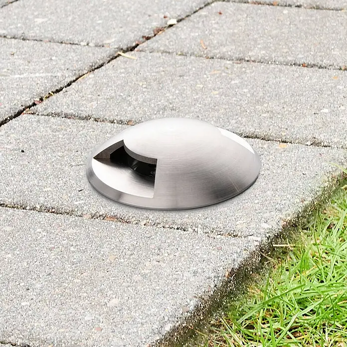 Lucande LED-Gartenstrahler Helene - 3.000 K, 8,8 x 8,8 x 9,5 cm - Gebürstete Edelstahl-Kuppel-Außenleuchte in einem gepflasterten Weg neben Gras installiert.