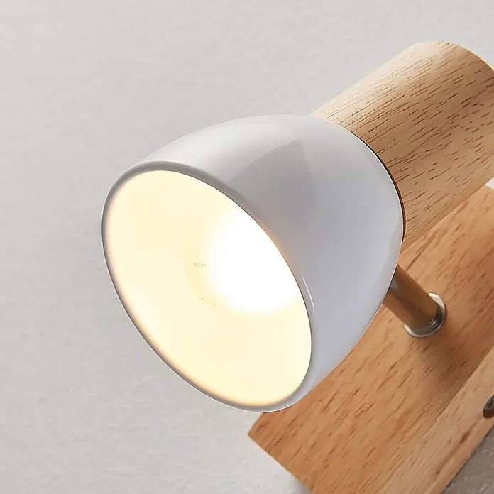 Lindby Wandstrahler Thorin - Holz hell, E14 - Ein wandmontierter Strahler mit weißem Metallschirm und hellem Holzsockel, der warmes Licht abgibt.