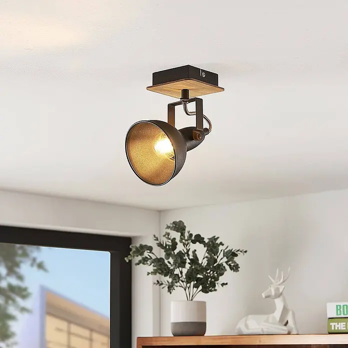 Lindby Wandstrahler Aylis - Holz dunkel, schwarz, E14 - Industrieller Deckenstrahler mit dunklem Metallschirm und Holzsockel, beleuchtet einen Raum.