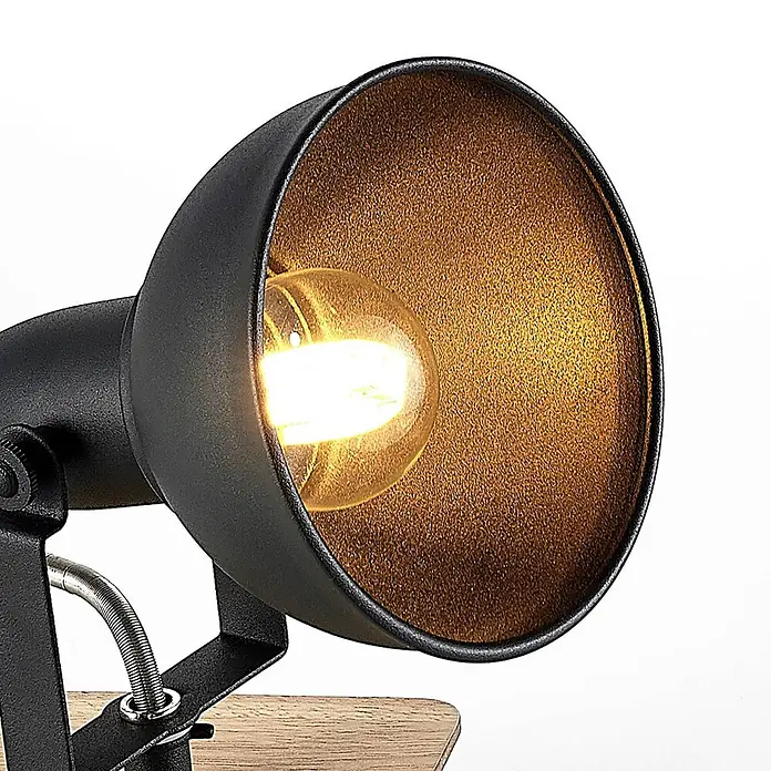Lindby Wandstrahler Aylis - Holz dunkel, schwarz, E14 - Nahaufnahme einer schwarzen Metall-Schreibtischlampe mit beleuchteter Glühbirne und strukturiertem goldenem Innenreflektor. Teilweise sichtbarer Holzsockel.