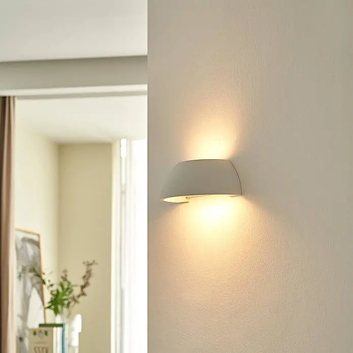 Lindby Wandleuchte Felia - L x B x H: 12 x 24,5 x 9 cm, weiß / opal, E14 - Gekrümmte, helle Wandleuchte strahlt warmes Auf-/Ablicht an eine Wand im modernen Interieur.