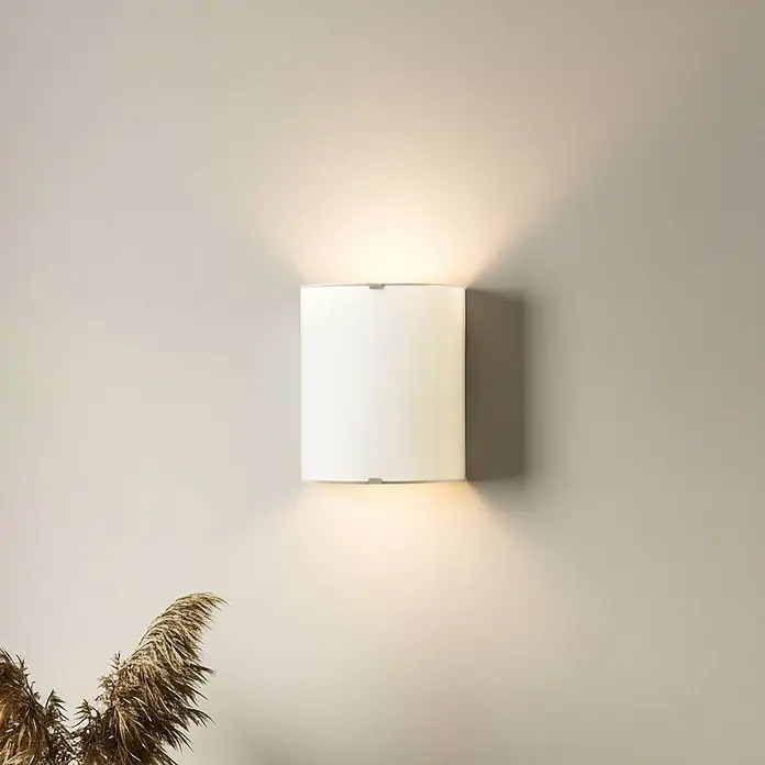 Lindby Wandleuchte Phil - weiß / opal, E27 - Weiße zylindrische Wandleuchte an einer Wand montiert, die warmes Licht nach oben und unten abgibt.