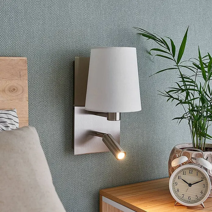 Lindby Wandleuchte Aiden - L x B x H: 17,6 x 14 x 30,8 cm, alu / grau / zink, weiß / opal, E14 - Gebürstete Metall-Wandleuchte mit weißem Stoffschirm und integrierter LED-Leselampe über einem Nachttisch.