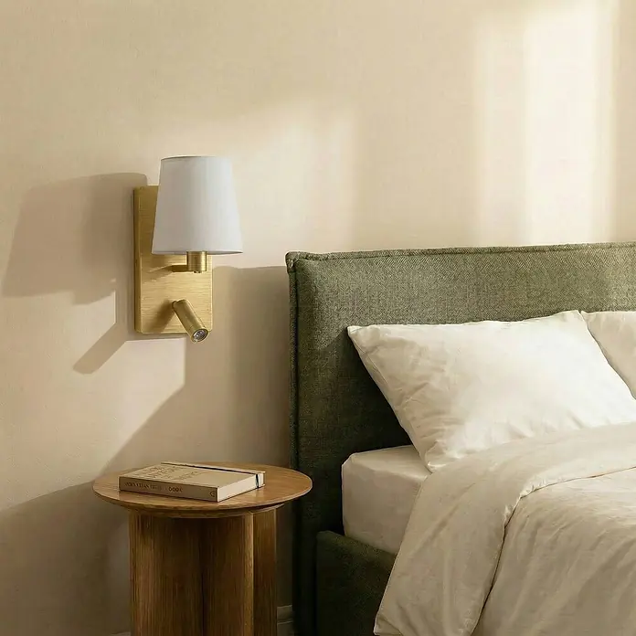 Lindby Wandleuchte Aiden - L x B x H: 17,6 x 14 x 30,8 cm, messing / gold, E14 - Messing-Wandleuchte mit weißem Schirm und integriertem Leselicht neben einem Bett mit Beistelltisch und Buch.