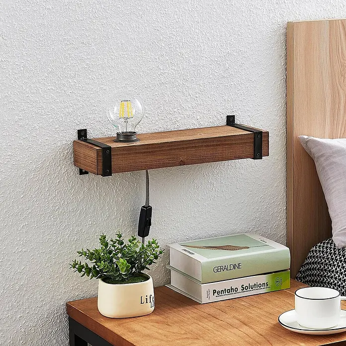 Lindby Wandleuchte Sverina - L x B x H: 12 x 40 x 10 cm, Holz dunkel, E27 - Rustikales Wandregal aus Holz mit schwarzen Metallhalterungen und Industriallampe, über einem Nachttisch mit Pflanze und Büchern positioniert.