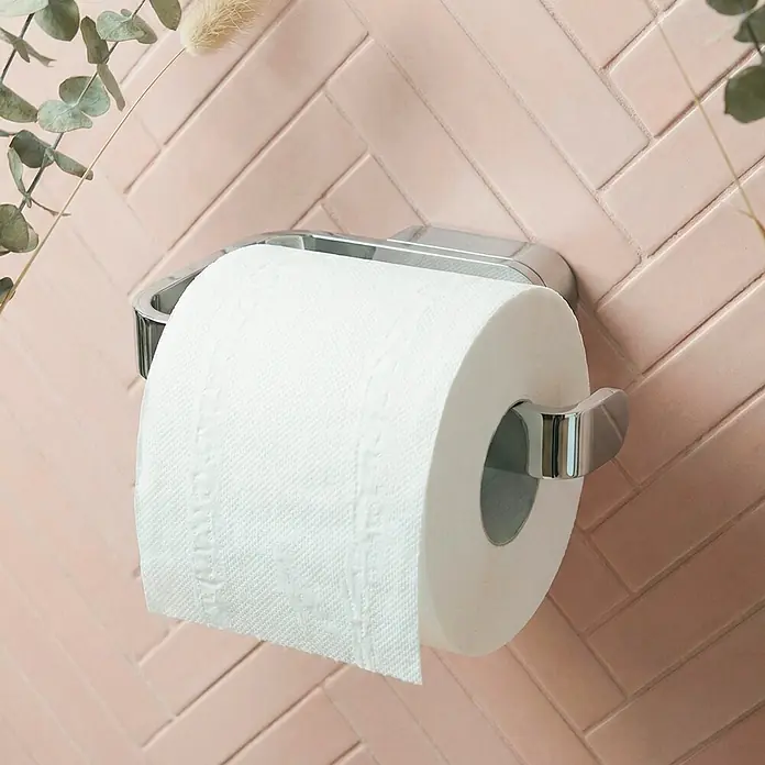 Lenz Aura Toilettenpapierhalter - Ohne Deckel, Chrom, Glänzend - Weiße Toilettenpapierrolle auf einem Chromhalter vor einer rosafarbenen Fischgrät-Fliesenwand.