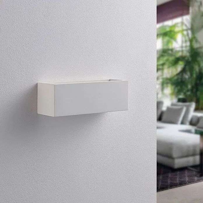 Lindby Wandleuchte Tjada - L x B x H: 7,5 x 21,8 x 7,5 cm, weiß / opal, G9 - Weißer rechteckiger Wandpflanzkasten an einer strukturierten Wand, mit einem unscharfen Wohnbereich im Hintergrund.